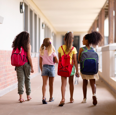A group of girls with backpacks walking down a hallway.